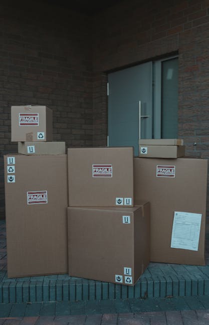 A man wearing a white t-shirt, jeans, and a black cap is seen loading three cardboard boxes into the side compartment of a white delivery van parked on a residential street. The van, which has a slidi